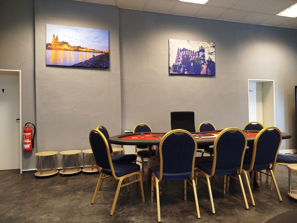 Ein Konferenzraum mit einem Tisch und blauen Stühlen; an der Wand hängen zwei Bilder.