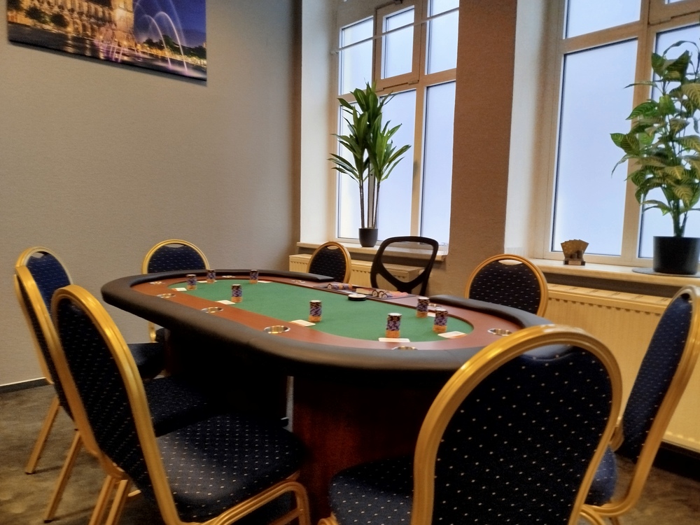 Ein leerer Pokertisch mit blauen Stühlen in einem Raum mit Pflanzen und Kunst an der Wand.