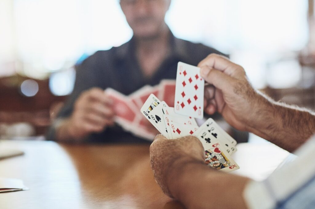 Kartenspiel, Spiel und Menschenhände im Seniorenheim mit Seniorenbetreuung, Spiel und Spaß am Tisch. Kognitiv, Gedächtnis und Aktivität in Freundeskreis mit Hobby, Entspannung und Poker für Gehirnaktivität und Unterstützung